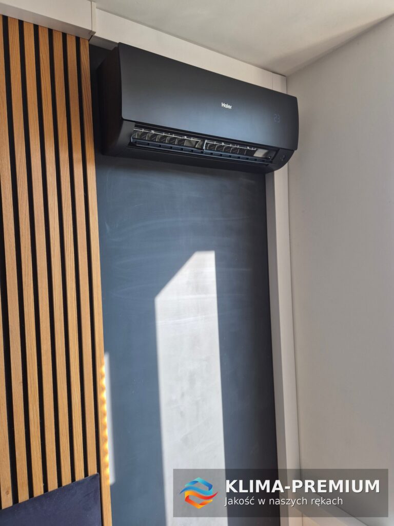 Czarny klimatyzator Haier 2,5 kW na grafitowej ścianie przy dębowych lamelach – montaż Klima-Premium, Mokotów Warszawa